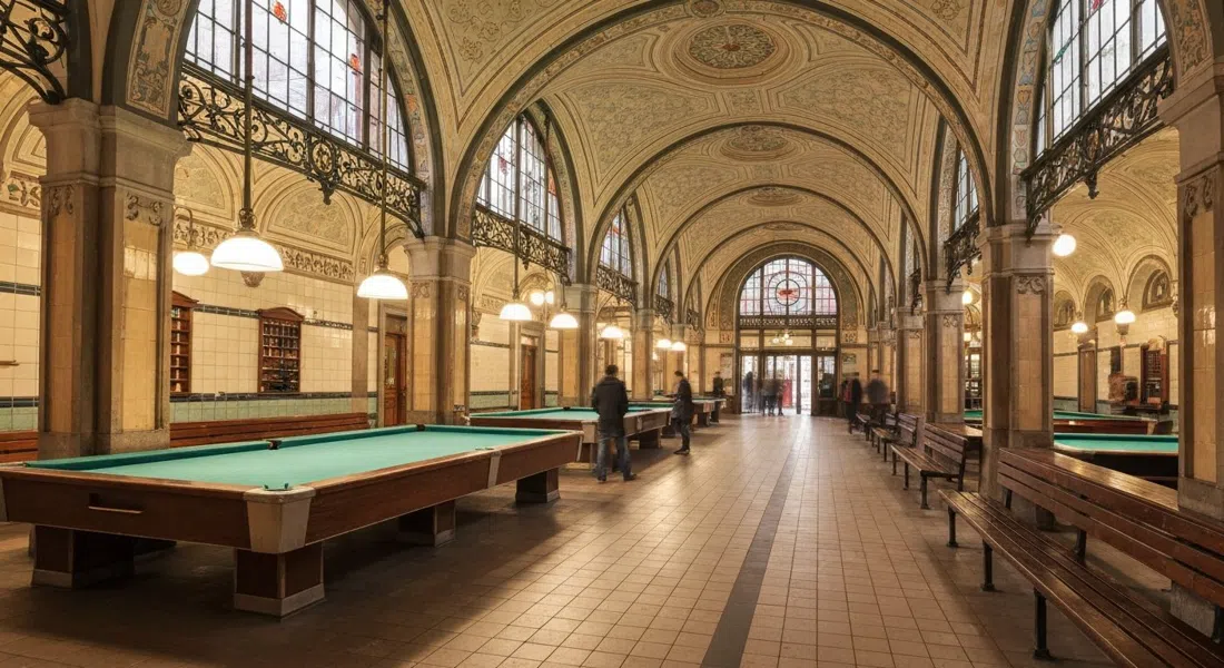 Interior del Müller'sches Volksbad, sala de piscina abovedada Art Nouveau con luz cálida sobre superficies de azulejos y elegante trabajo en hierro